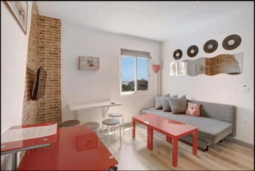 Moderno estudio en Santa Cruz de Tenerife con sofá gris, mesa roja, chimenea de ladrillo y balcón con vista al mar.