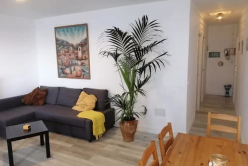 Sala de estar moderna en Tenerife con sofá oscuro, mesa de comedor de madera, planta de palma en maceta y cuadros decorativos