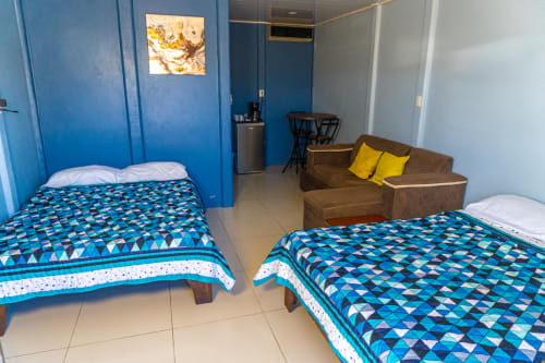 Habitación luminosa en Cabinas Arenal Home con dos camas, área de estar marrón, paredes azules y piso de baldosas en San Carlos, Costa Rica