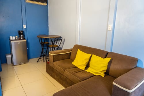 Sofá marrón con cojines amarillos en habitación de paredes azul brillante en Cabinas Arenal Home, Costa Rica, con mini nevera