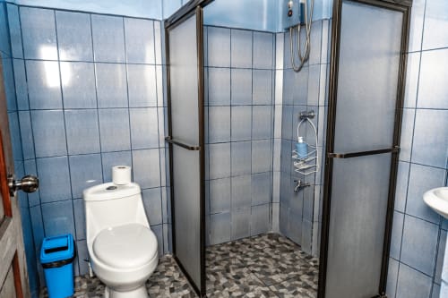 Baño con paredes de azulejos azules, inodoro blanco y ducha con cristal en el hotel Cabinas Arenal Home, Costa Rica