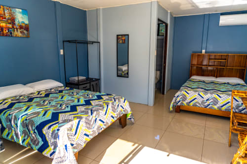 Espaciosa habitación cuádruple en Cabinas Arenal Home con dos camas, paredes azules, muebles de madera y aire acondicionado en San Carlos
