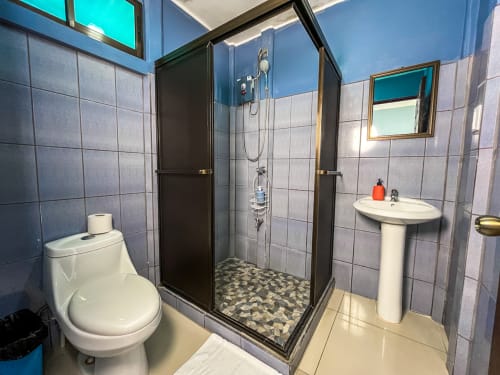 Moderno baño en Cabinas Arenal Home con ducha de marco negro, inodoro blanco, lavamanos pedestal y paredes de azulejos azules