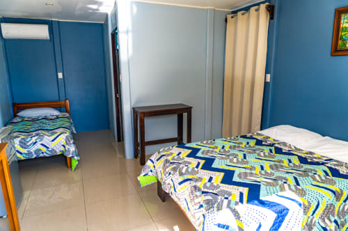Habitación azul brillante en Cabinas Arenal Home con dos camas, muebles de madera y aire acondicionado en Costa Rica
