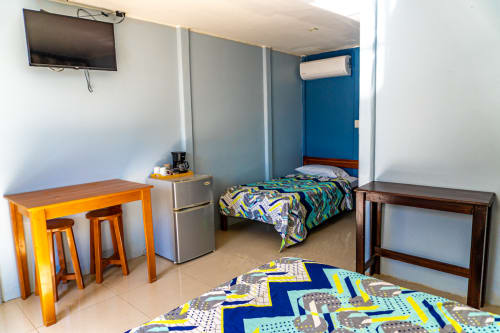 Amplia habitación triple en Cabinas Arenal Home con dos camas coloridas, mesa de comedor amarilla, refrigerador, TV y aire acondicionado