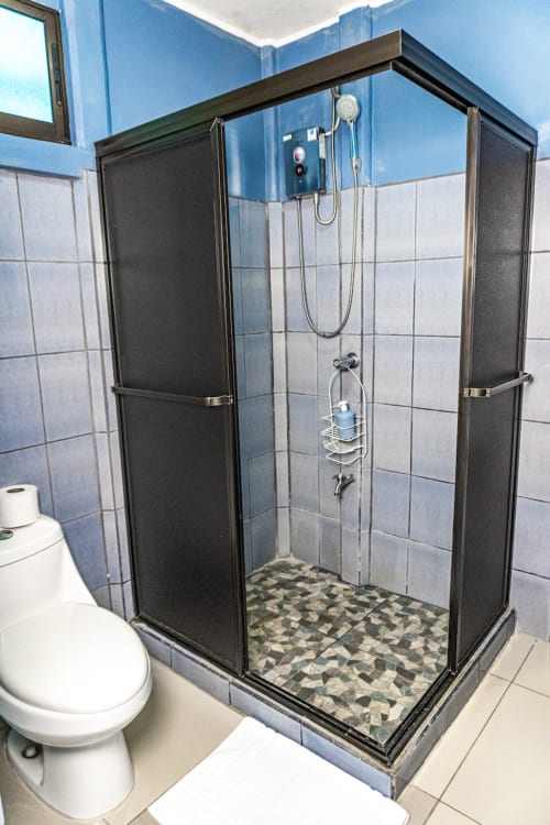 Moderno baño con puertas de cristal negro y piso de azulejos decorativos en habitación del hotel Cabinas Arenal Home, Costa Rica