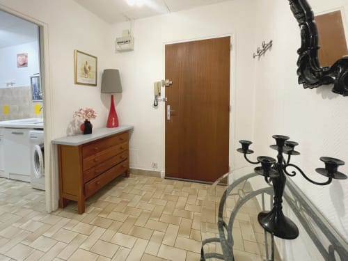 Couloir d'entrée du Studio MISTRAL avec commode en bois, lampe rouge et candélabre noir dans l'appartement de Digne-les-Bains