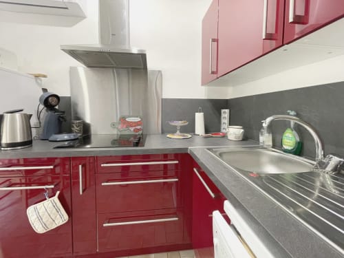 Cuisine moderne du Studio MISTRAL au Vallon des Sources à Digne-les-Bains, avec armoires rouges et électroménagers en acier inoxydable