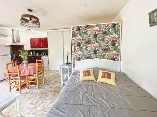 Appartement Studio MISTRAL à Digne-les-Bains : lit, kitchenette, coin repas et tête de lit papier peint tropical