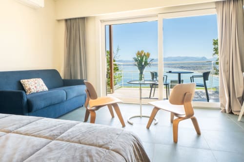 Junior suite del Belvedere Resort con balcone vista mare su Castellammare del Golfo, divano blu e sedie in legno