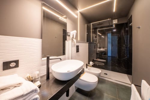 Bagno moderno presso Hotel Belvedere Resort con lavabo vessel, dettagli in marmo nero, specchio illuminato e doccia in vetro