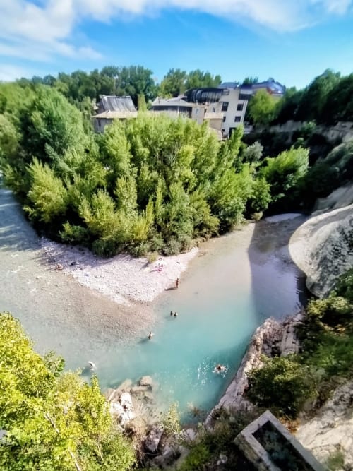 Türkiser Fluss mit Sandstrand und üppiger Vegetation, Steingebäude zwischen Bäumen in Gagnières, Südfrankreich