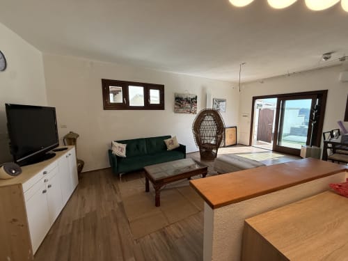 Ampio soggiorno con vista mare in Sardegna: divano verde, arredamento in legno, TV, accesso terrazza
