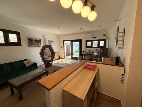 Luminosa zona living open-plan in appartamento Sardegna Holidays con isola cucina, divano verde, sedia intrecciata e vista mare