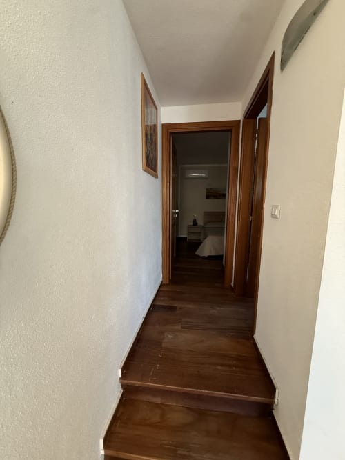 Corridoio dell'appartamento in Sardegna con porte in legno, pareti bianche, pavimento in legno scuro che conduce alla camera da letto con vista sul mare
