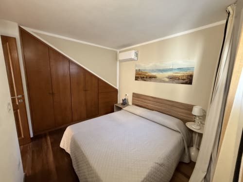 Camera moderna a Sardinia Holidays con letto matrimoniale, guardaroba in legno, opera d'arte con vista marina e suggestiva atmosfera balneare a Torpè