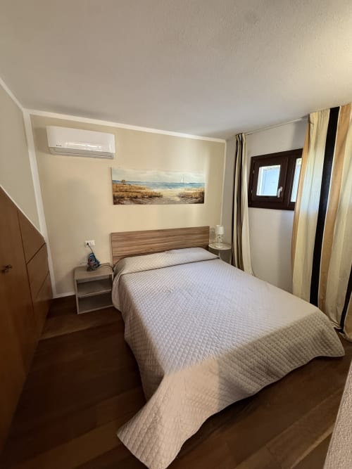 Camera luminosa con letto matrimoniale, quadri con vista mare, climatizzatore e pavimenti in legno scuro nell'appartamento Sardinia Holidays, Torpè