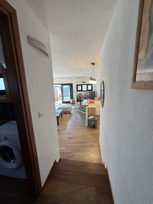 Vista del corridoio dell'appartamento con vista mare in Sardegna con cucina e zona living visibili, pavimenti in legno
