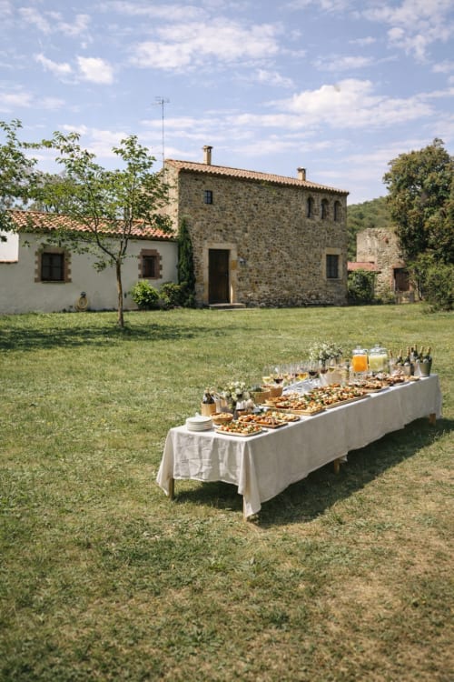 Outdoor dining setup at Molí Roquer guesthouse in Rabós with rustic stone buildings and green lawn