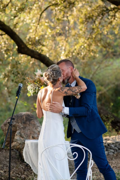 Bride and groom kiss at outdoor wedding ceremony under tree at Molí Roquer, Rabós