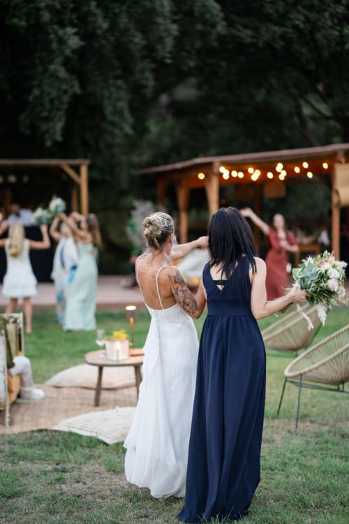 Bride and bridesmaid at outdoor wedding reception at Molí Roquer in Rabós with string lights and garden setting