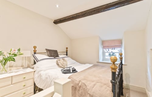 Cosy bedroom in Crickhowell cottage with metal bed frame, exposed wooden beam, white bedding, and mountain view window