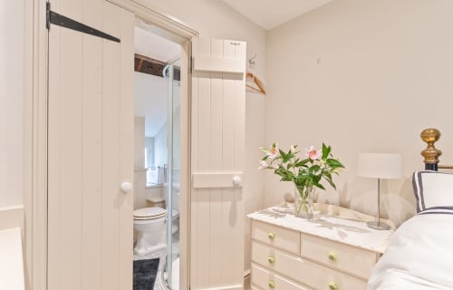 Cosy Llangattock Hideaway cottage bedroom with en-suite bathroom, fresh flowers, lamp, and dresser with brass handles
