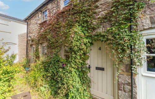 Ivy-covered stone cottage entrance with cream door at Cosy Crickhowell Cottage, Crickowell