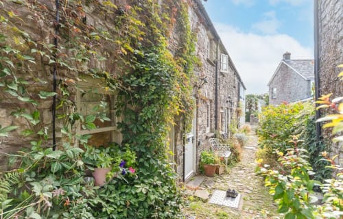 Charming stone cottage in Crickhowell with ivy-covered walls, flowering plants, and a rustic pathway leading to other