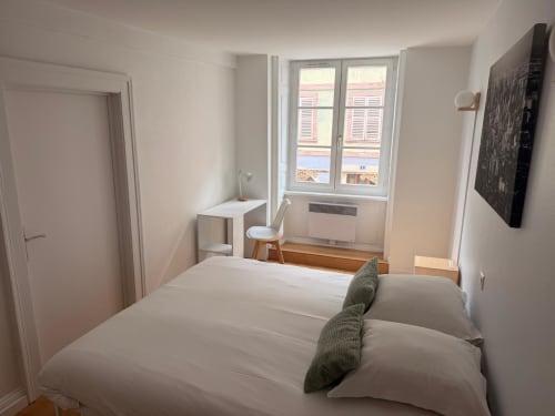 Chambre lumineuse de l'appartement de Belfort avec lit double, bureau, fenêtre sur la ville et équipements modernes