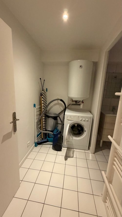 Buanderie de l'appartement de Belfort avec machine à laver, chauffe-eau et produits d'entretien sur sol carrelé