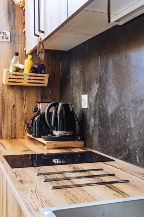 Kitchenette moderne aux comptoirs en bois, plaque de cuisson à induction noire, bouilloire électrique et mur texturé foncé à Cocon De