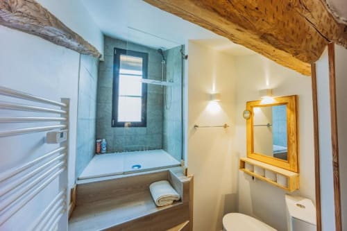 Salle de bain moderne au Cocon De Roussillon avec douche carrelée bleue, poutres bois et miroir encadré bois
