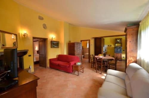 Luminosa sala living gialla con divano rosso, zona pranzo e arredi in legno presso l'appartamento Il Tiglio di Agriturismo Buriano