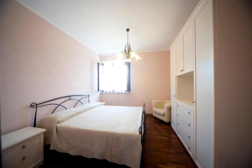 Camera spaziosa nell'appartamento L'Elce di Agriturismo Buriano con letto in ferro battuto, armadio bianco e finestra con vista sul giardino