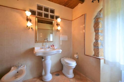 Bagno elegante dell'Agriturismo Buriano con lavabo su piedistallo, toilet, bidet e specchio con applique