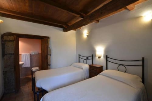 Camera doppia con travi in legno rustico, letti in ferro, biancheria bianca e bagno privato nell'appartamento Il Tiglio
