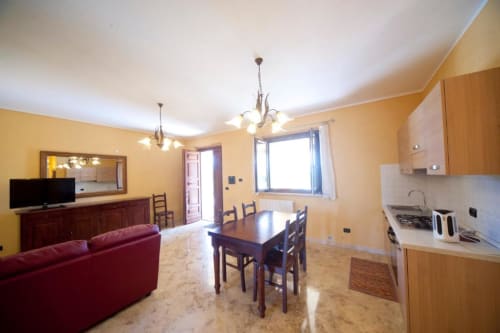 Luminosa zona living open-plan dell'appartamento L'Elce a Lubriano con pareti gialle, cucina, tavolo da pranzo e divano rosso