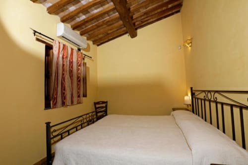 Camera luminosa giallo sole nella villa Il Mandorlo di Agriturismo Buriano con letti gemelli, travi in legno e aria condizionata.
