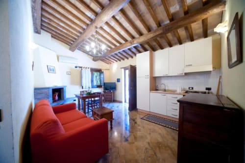 Ampio soggiorno open-plan nello chalet Il Mandorlo con divano rosso, camino, cucina bianca, soffitto con travi in legno