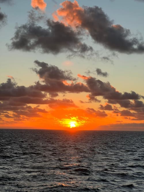 Stunning ocean sunset with vibrant orange sky and dramatic clouds over calm sea at Malkita Homes, Highland Mills