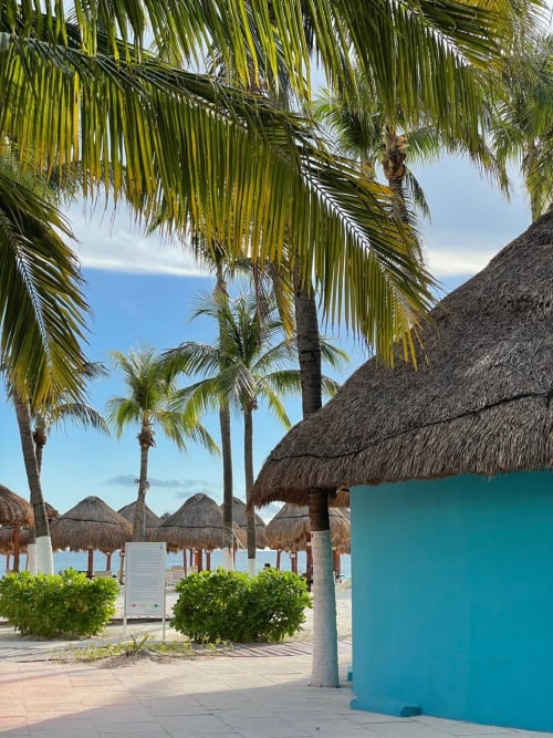 Tropical beach resort with thatched-roof palapas, palm trees, and turquoise buildings at Malkita Homes