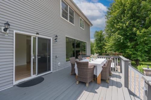 Outdoor deck at Malkita Homes in Highland Mills with dining table, wicker chairs, and views of lush green trees.