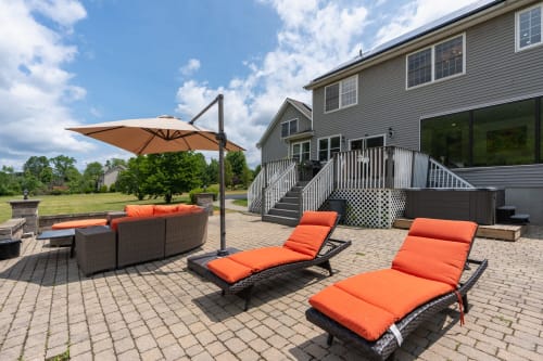 Outdoor patio at Malkita Homes Highland Mills with lounge chairs, orange cushions, and cantilever umbrella overlooking lawn