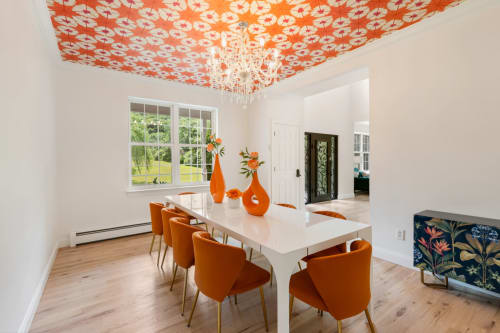 Modern dining room at Malkita Homes with orange patterned ceiling, white table, orange chairs, and large windows overlooking