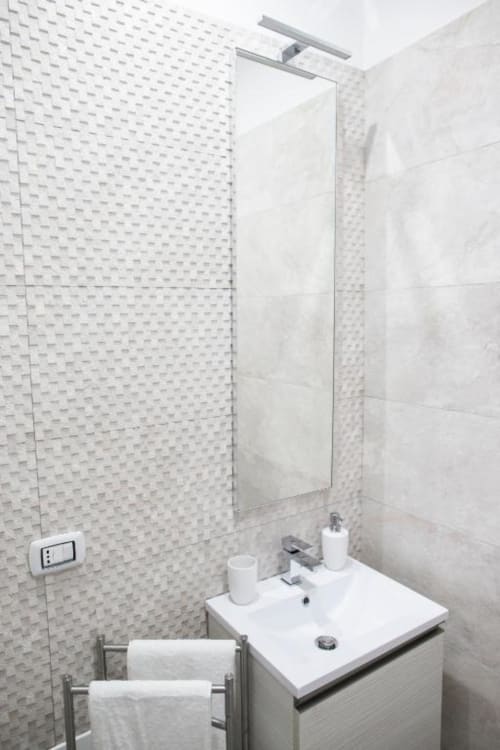 Moderno bagno della King Deluxe Room di Roma's Domus Gaudia con piastrelle bianche texture, specchio, lavabo e portasciugamani