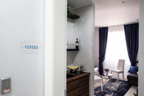 Ingresso della Junior Family Suite presso l'Exclusive Domus Gaudia Rome, con angolo cottura e zona living con tende blu e arredo moderno