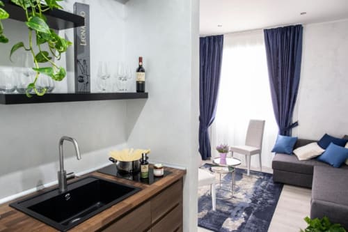 Piccola cucina e zona living della Junior Family Suite presso l'Exclusive Domus Gaudia a Roma, con tende blu e divano