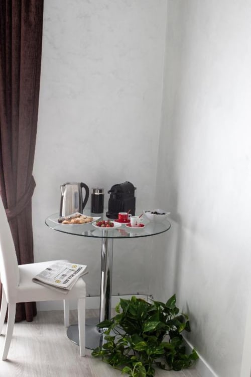 Modern hotel room corner at Domus Gaudia Roma with round glass table, electric kettle, pastries, fresh berries, and green