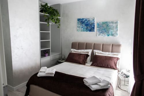 Camera da letto moderna presso Exclusive Domus Gaudia a Roma con testata beige, cuscini borgogna e arte astratta blu a parete